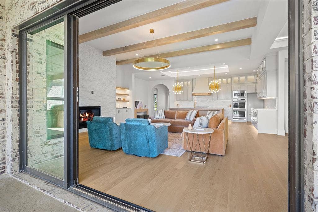 3333 Bridgegate Avenue, Northlake, TX 76247 Sliding glass doors opening to a living area featuring wood-finish flooring, exposed ceiling beams, a built-in fireplace, and a kitchen with integrated appliances