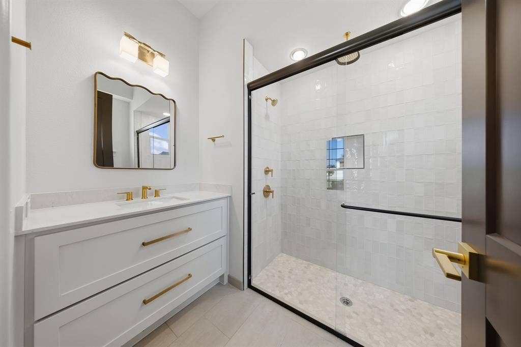 3333 Bridgegate Avenue, Northlake, TX 76247 White shaker vanity with quartz countertop, gold-finish hardware, and a frameless glass shower enclosure featuring a tiled interior