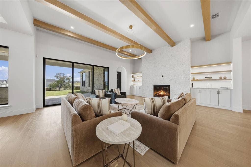 3333 Bridgegate Avenue, Northlake, TX 76247 Vaulted ceiling with exposed wood beams, expansive sliding glass doors, white brick fireplace, built-in shelving, and wood-finish flooring
