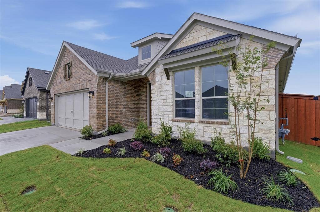 15056 Green Bluff Drive, Aledo, TX 76008 Stone and brick exterior featuring a multi-pane window, landscaped front beds, an attached garage, and a concrete driveway