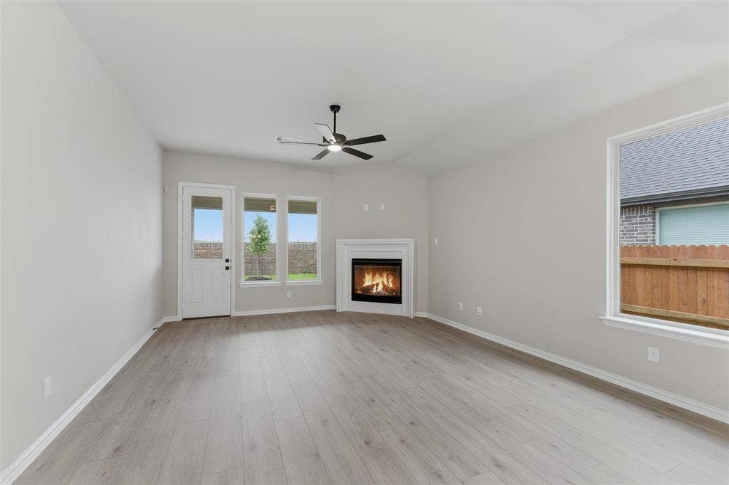 15056 Green Bluff Drive, Aledo, TX 76008 Spacious interior featuring a corner fireplace with white mantel, a ceiling fan with integrated lighting, wood-finish flooring, and multiple windows providing natural light