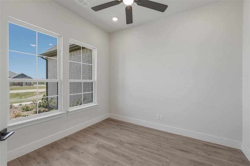 12117 Clastic Court, Krum, TX 76249 Light-filled room featuring two multi-pane windows, wood-finish flooring, a ceiling fan with integrated lighting, and recessed ceiling lights