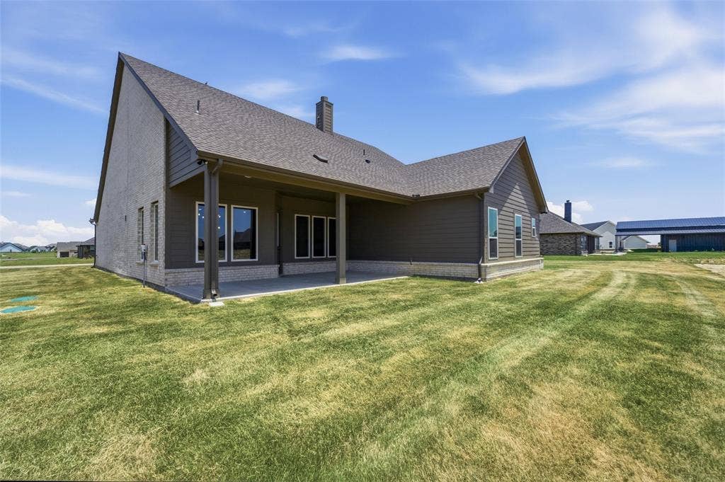 12117 Clastic Court, Krum, TX 76249 Rear exterior featuring an expansive concrete patio, covered porch area with support columns, and multiple windows