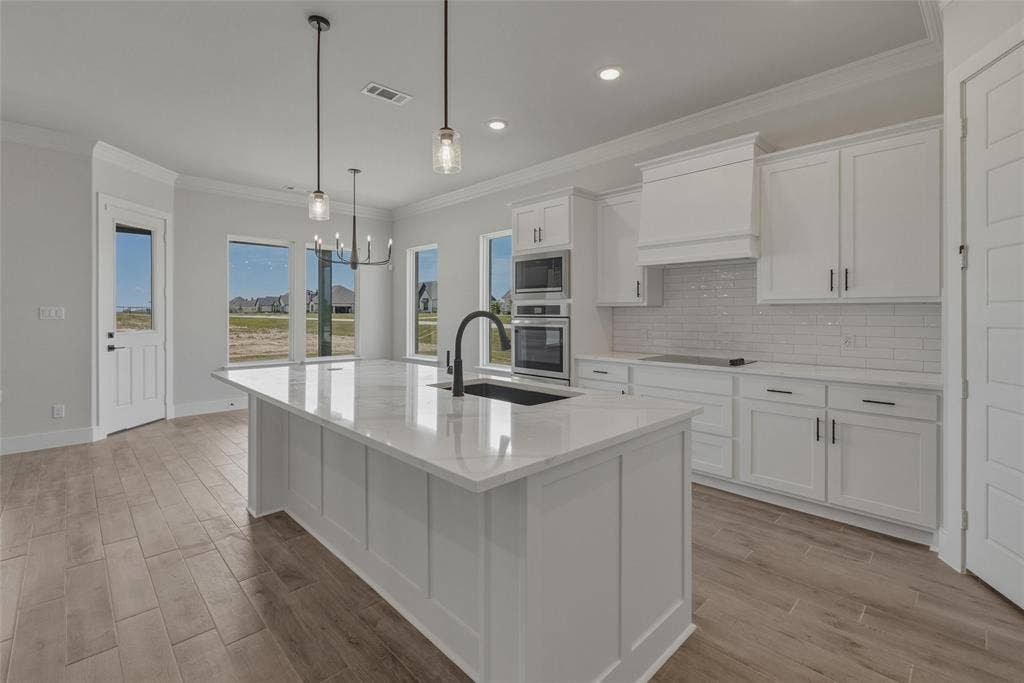 12117 Clastic Court, Krum, TX 76249 Modern kitchen featuring an expansive center island with a white countertop and integrated sink, white shaker cabinetry, stainless steel built-in appliances, and wood-finish flooring