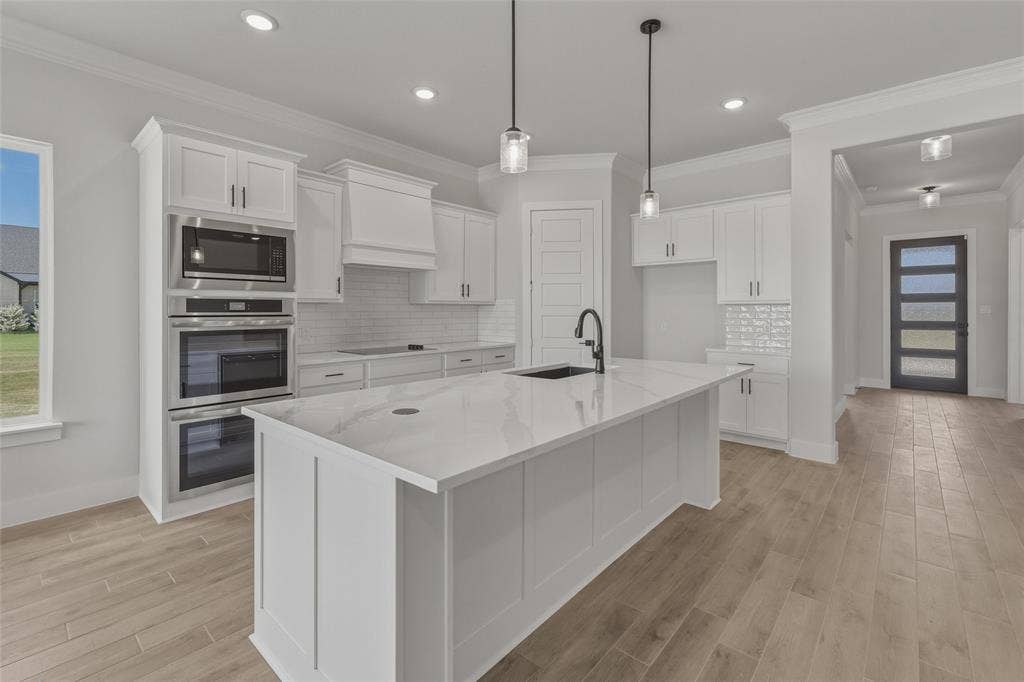 12117 Clastic Court, Krum, TX 76249 Kitchen featuring a large central island with a sink, white cabinetry, integrated stainless steel appliances, and wood-finish flooring