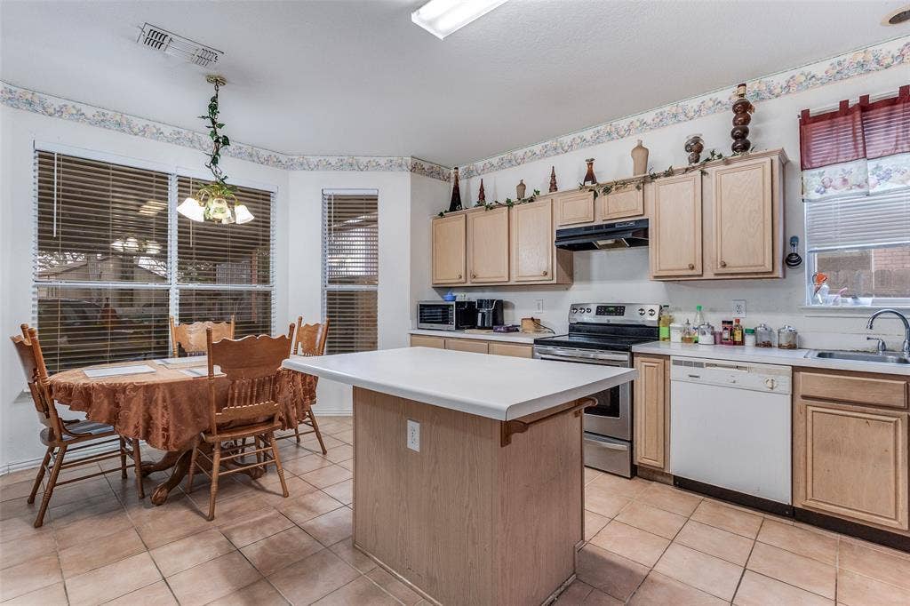 Kitchen with stainless steel range with electric cooktop, light countertops, light wood finish cabinets, white dishwasher, and a kitchen island