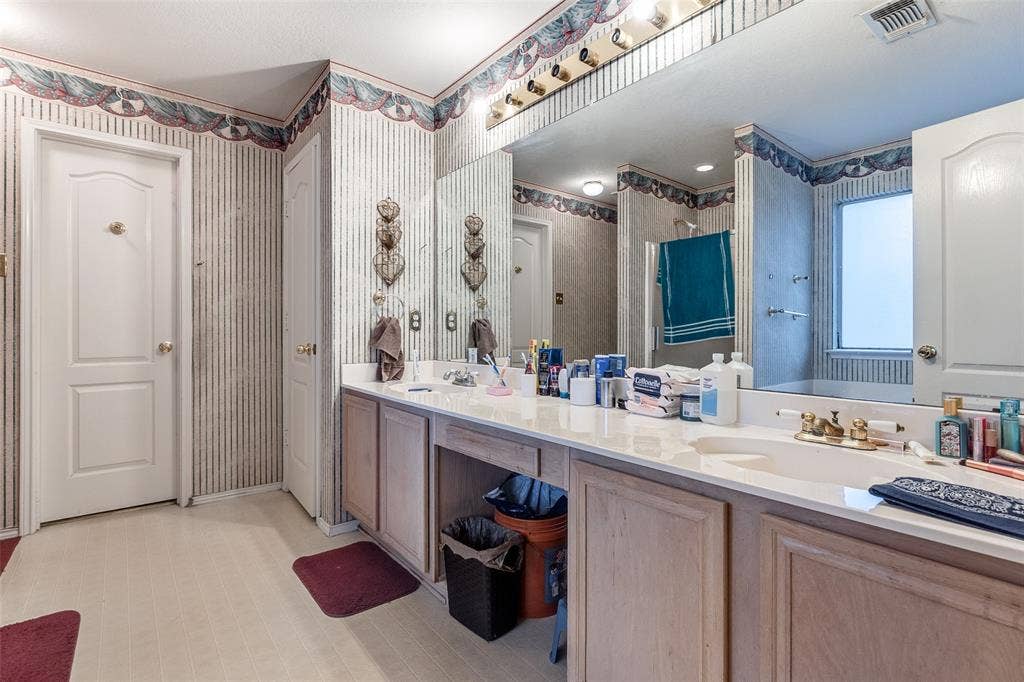 Full bathroom with double vanity, wallpapered walls, and a stall shower