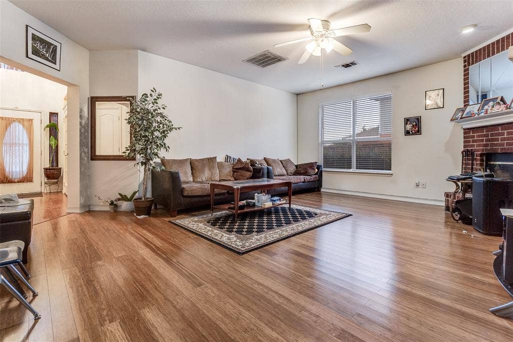 Living room with ceiling fan, wood finished floors, and a brick fireplace
