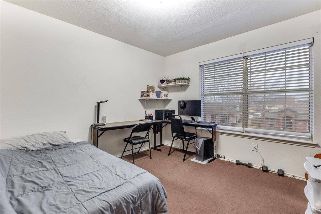 Bedroom featuring light colored carpet, an office area, and a textured ceiling