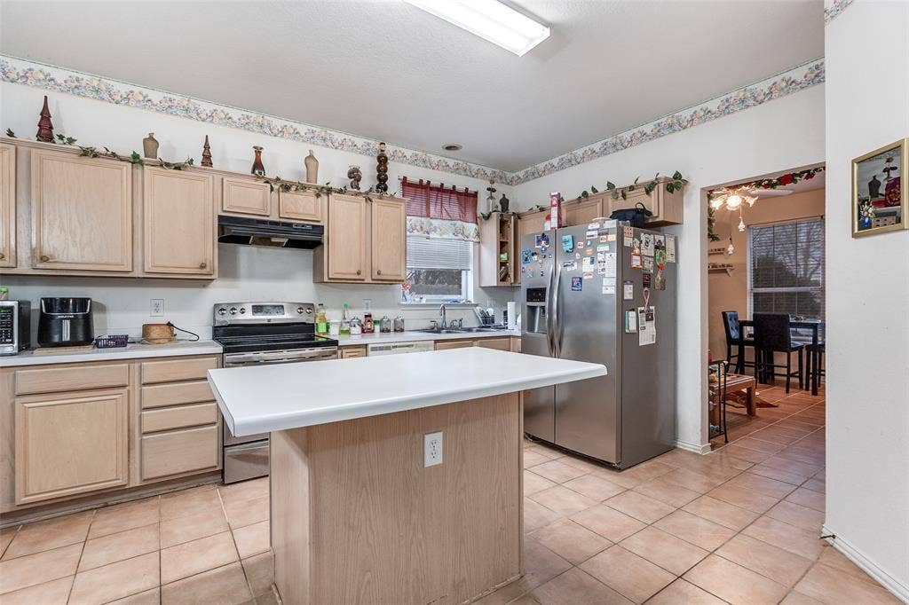 Kitchen featuring stainless steel appliances, light wood finish cabinets, light countertops, a kitchen island, and light tile patterned flooring