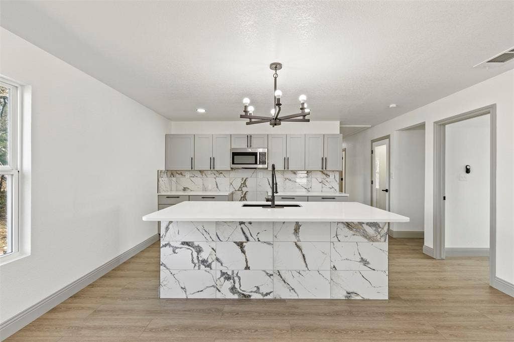 5619 Lake Granbury Trail, Granbury, TX 76048 Kitchen featuring a center island with sink, light wood-type flooring, gray cabinetry, suspended lighting, and stainless steel microwave