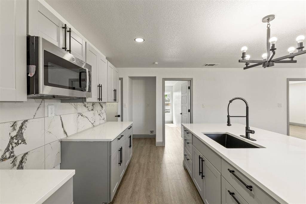 5619 Lake Granbury Trail, Granbury, TX 76048 Kitchen with stainless steel microwave, gray cabinetry, light stone countertops, light wood-style floors, and a textured ceiling