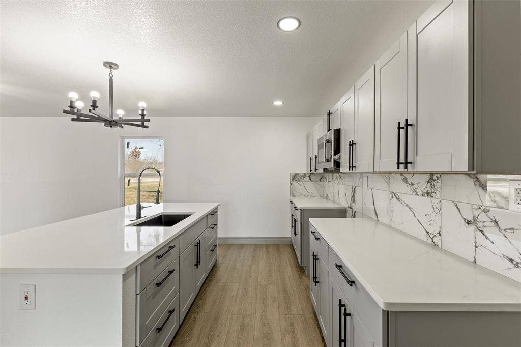 5619 Lake Granbury Trail, Granbury, TX 76048 Kitchen featuring light wood-style floors, an island with sink, light stone countertops, gray cabinets, and a textured ceiling