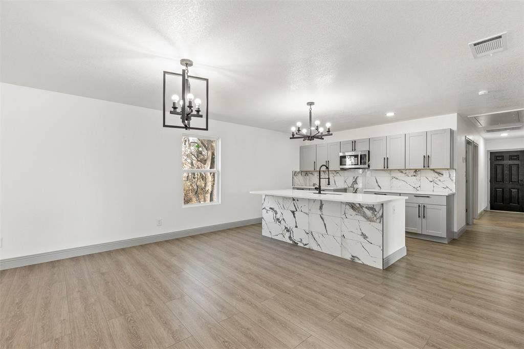 5619 Lake Granbury Trail, Granbury, TX 76048 Kitchen with gray cabinetry, a center island with sink, stainless steel microwave, and a chandelier
