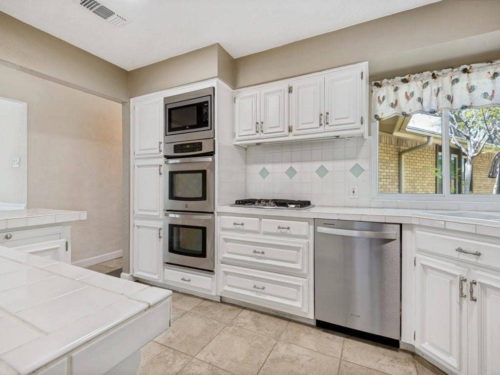 108 Wellesley Drive, Irving, TX 75062 Kitchen featuring stainless steel appliances, white cabinetry, decorative backsplash, and light tile patterned floors