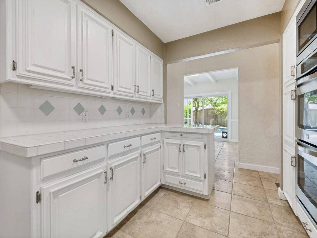 108 Wellesley Drive, Irving, TX 75062 Kitchen featuring tile counters, white cabinetry, backsplash, stainless steel appliances, and light tile patterned floors