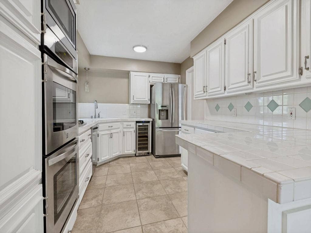 108 Wellesley Drive, Irving, TX 75062 Kitchen with a peninsula, white cabinetry, stainless steel appliances, beverage cooler, and tasteful backsplash