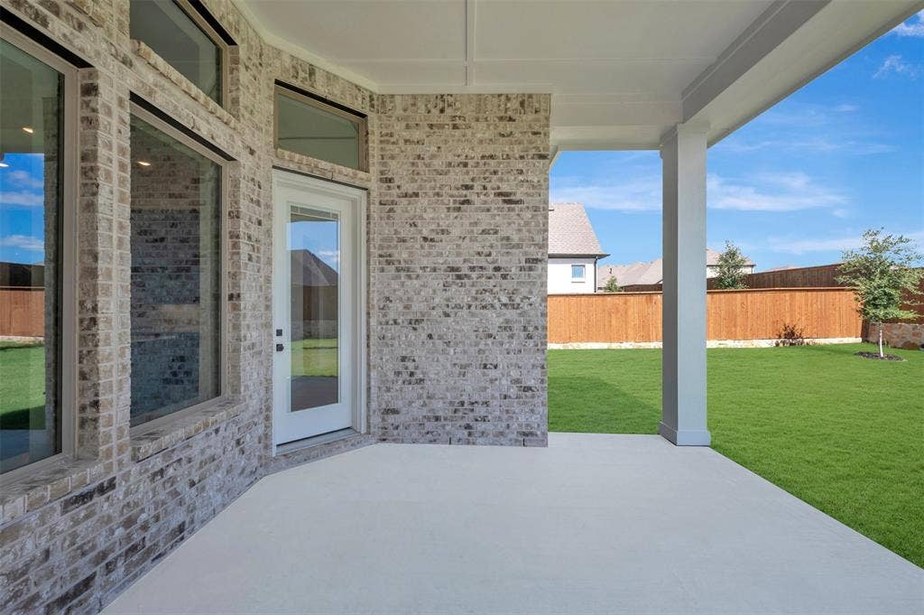 Expansive covered patio featuring a concrete surface, white support columns, and a brick exterior facade