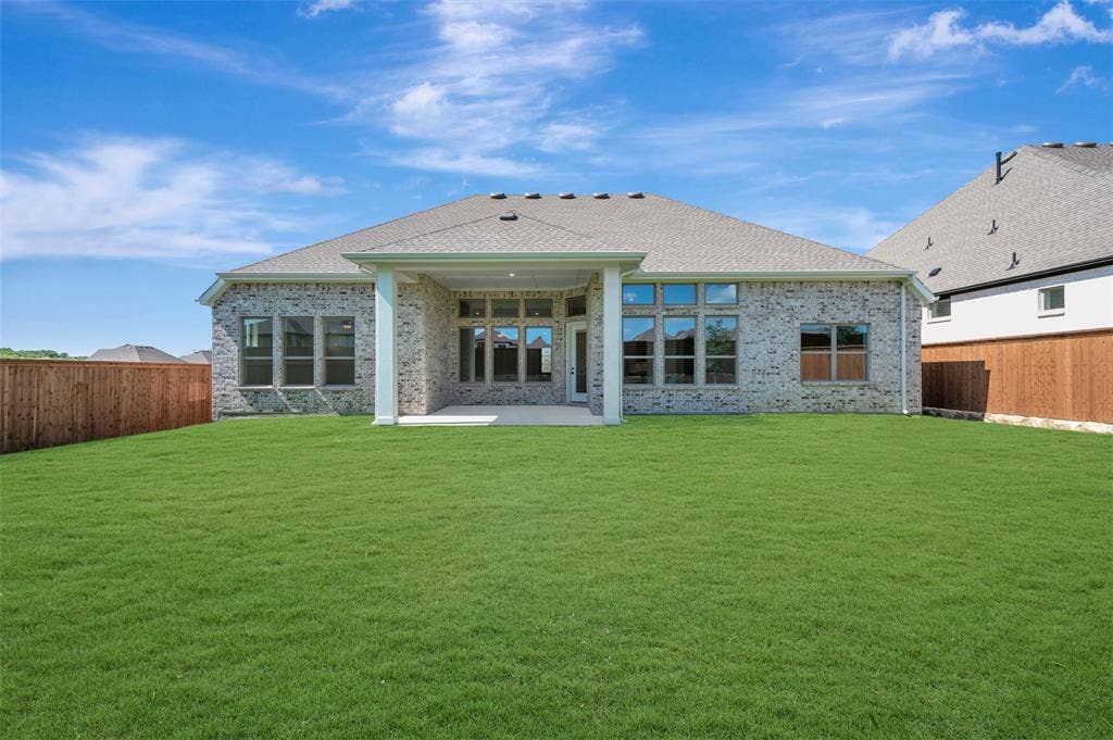 Expansive backyard featuring a large grass lawn, privacy fencing, and a covered concrete patio
