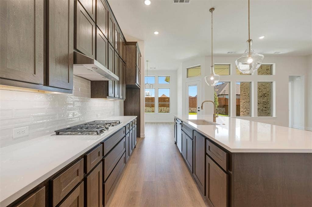 Contemporary kitchen featuring dark wood cabinetry, white countertops, a gas range with a sleek vent hood, and a large island with a stainless steel sink and modern faucet