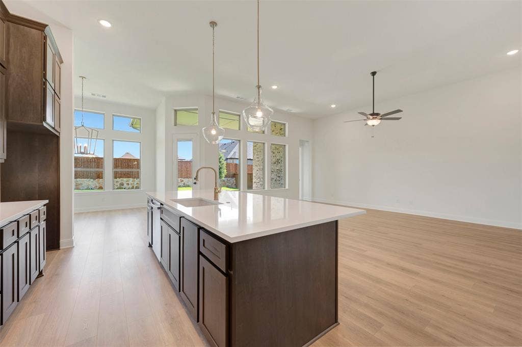 Open-concept kitchen and living area featuring a large center island with a sink, pendant lighting, wood-finish flooring, recessed lighting, and a ceiling fan