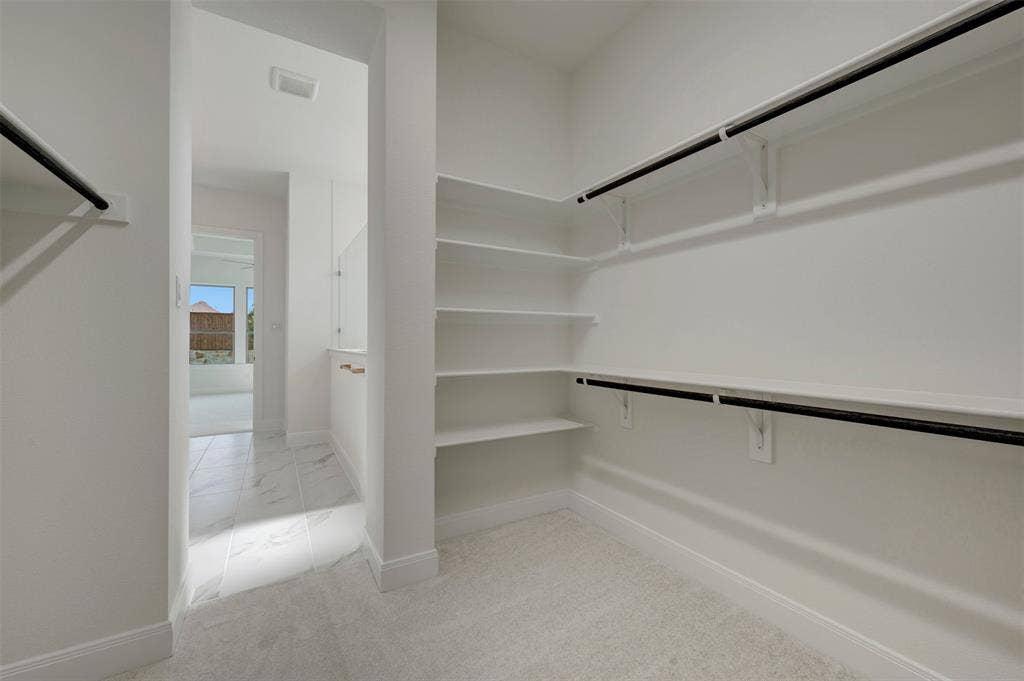 Spacious walk-in closet featuring extensive built-in shelving, dual hanging rods, light-toned carpeting, and crisp white walls