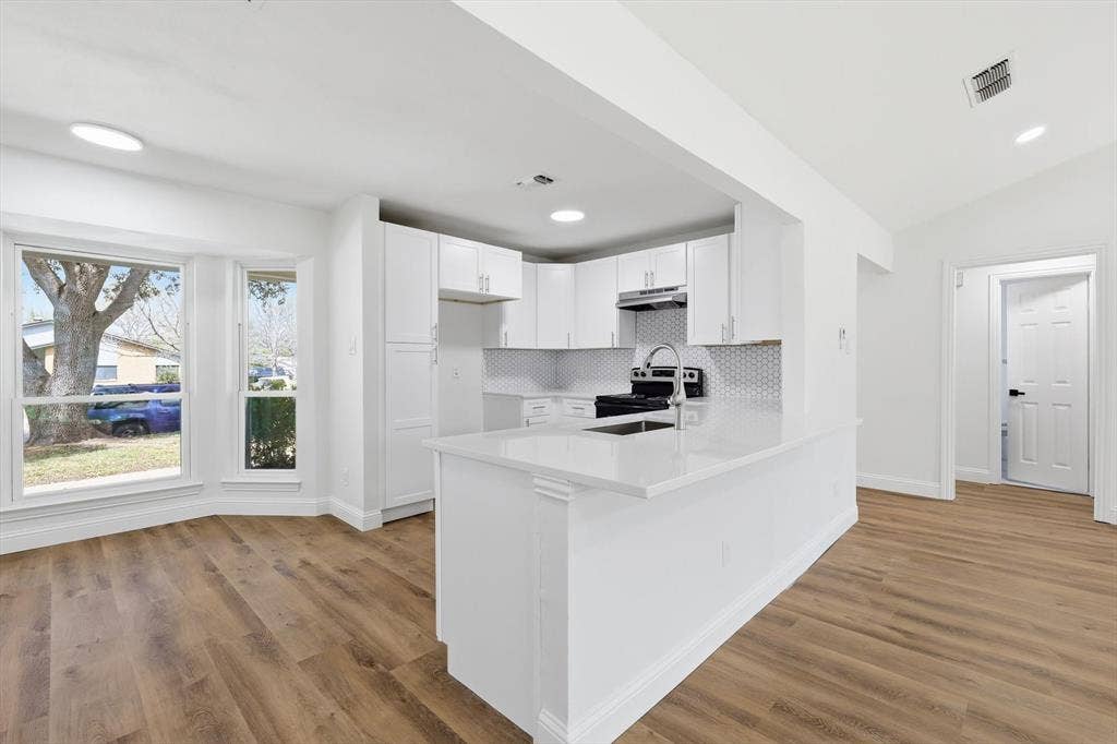 2211 Sierra Drive, Grapevine, TX 76051 Kitchen featuring a peninsula, stainless steel electric range, white cabinets, light wood finished floors, and vaulted ceiling