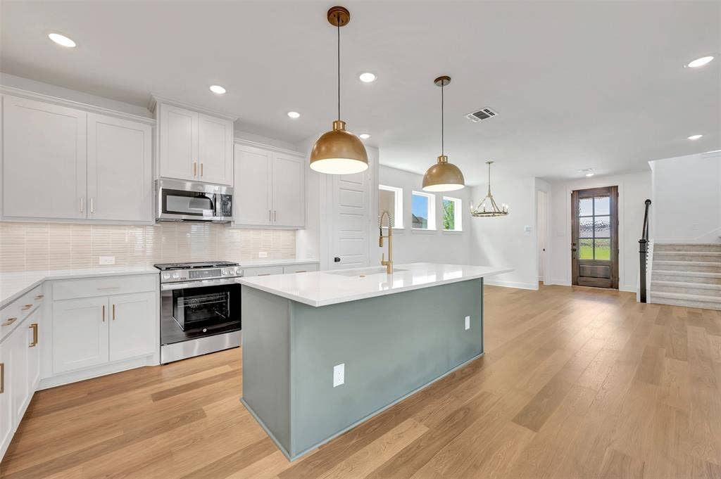 4721 Vizsla Lane, McKinney, TX 75071 Modern kitchen featuring a central island with a light teal base, white countertops, stainless steel appliances, white cabinetry, and wood-finish flooring