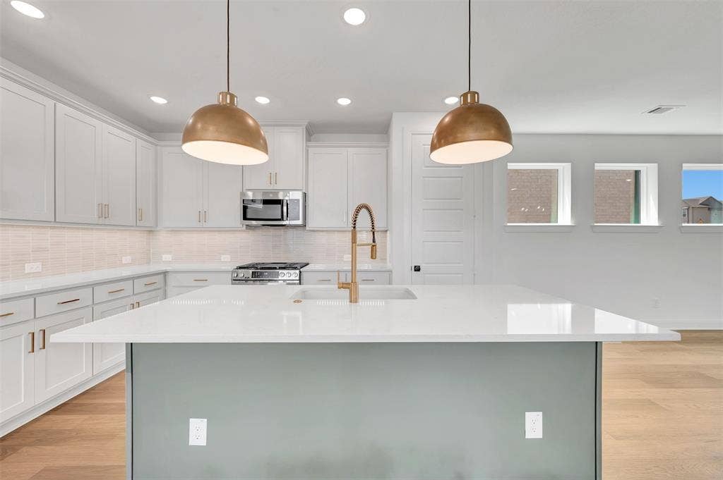 4721 Vizsla Lane, McKinney, TX 75071 Spacious kitchen featuring a large island with a light-colored countertop, white cabinetry with gold-toned hardware, a stainless steel gas range, and two suspended gold-toned pendant lights