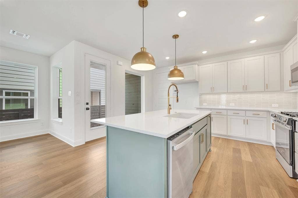 4721 Vizsla Lane, McKinney, TX 75071 Open-concept kitchen featuring light wood-finish flooring, a central island with a white countertop, two pendant light fixtures, white cabinetry, and stainless steel appliances