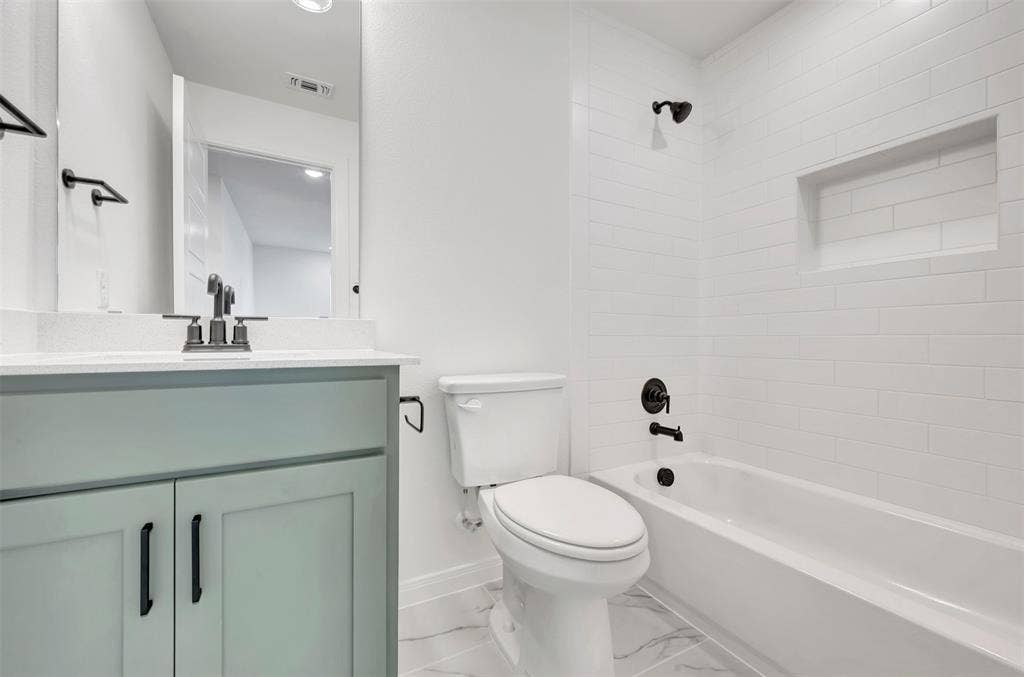 4721 Vizsla Lane, McKinney, TX 75071 Bathroom featuring a sage green vanity with a white countertop, matte black fixtures, subway tile tub surround with a recessed niche, and marble-look floor tiling