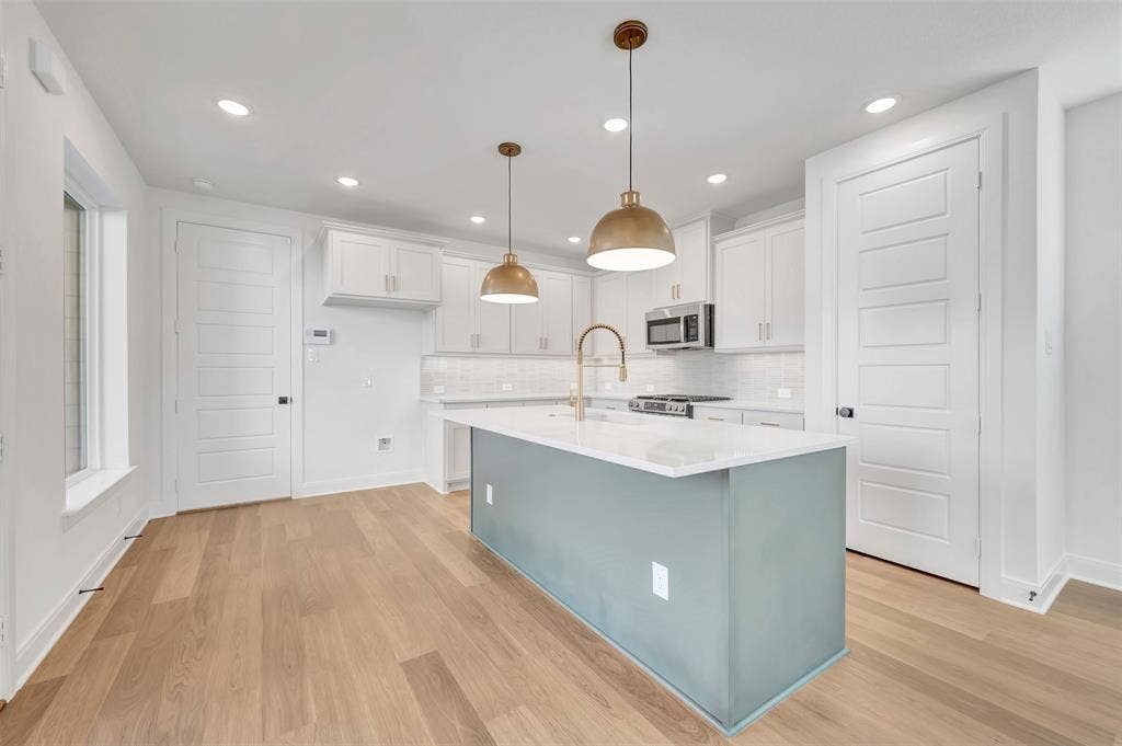 4721 Vizsla Lane, McKinney, TX 75071 Open-concept kitchen featuring a central island with a light blue-grey finish, white countertops, stainless steel appliances, white cabinetry, and wood-finish flooring