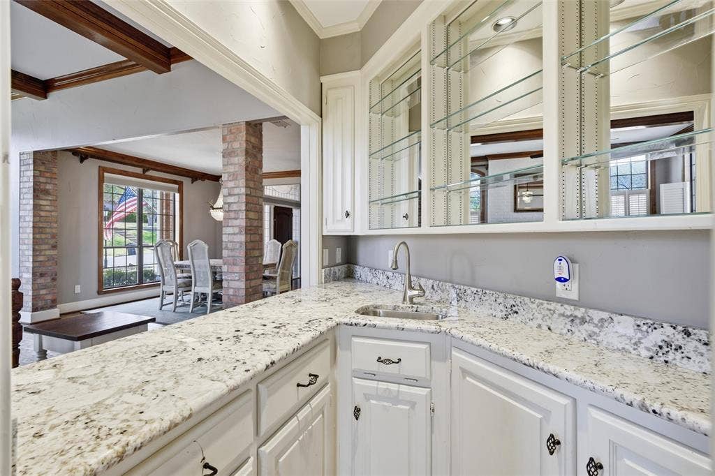 Wet Bar featuring ornamental molding, decorative columns, light stone countertops, and white cabinets