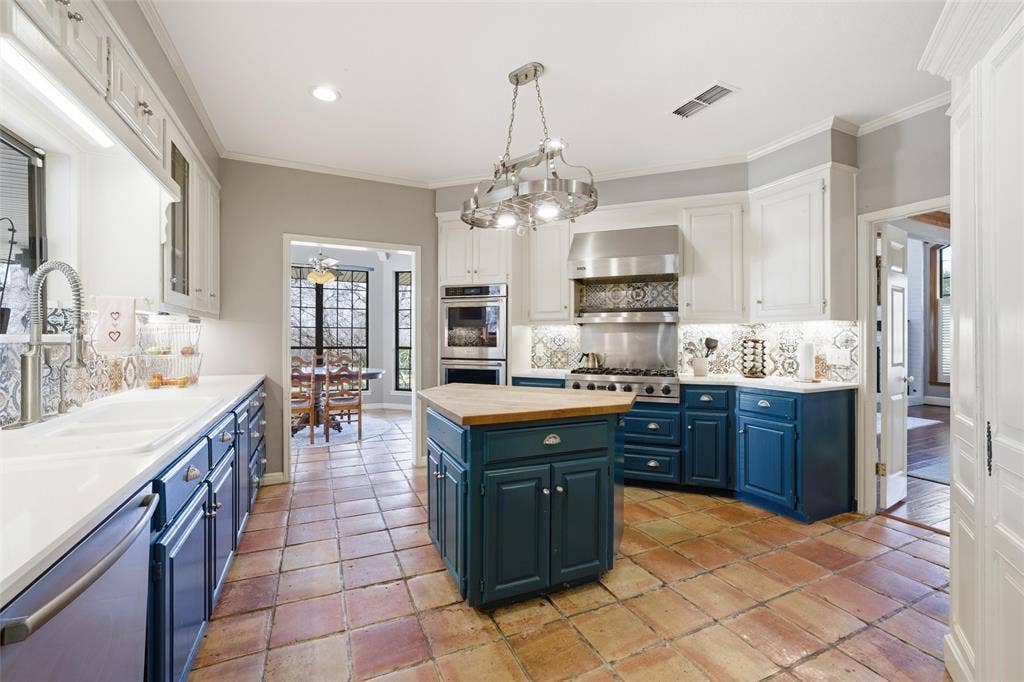 Kitchen featuring two tone cabinets, stainless steel appliances, pendant lighting, crown molding, and a center island