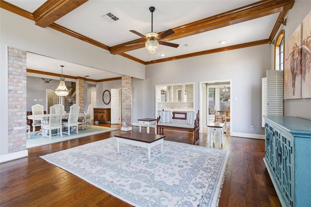 Living room featuring decorative columns, dark wood-type flooring, ceiling fan, and crown molding