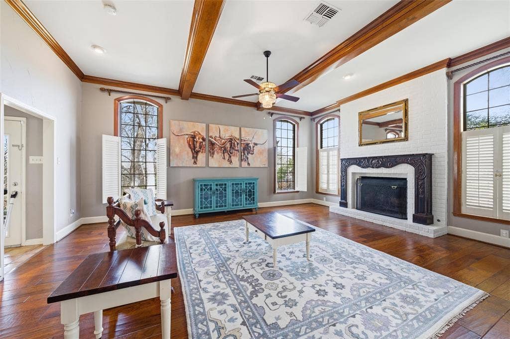 Living room featuring dark wood finished floors, a brick fireplace, ceiling fan, beamed ceiling, and ornamental molding