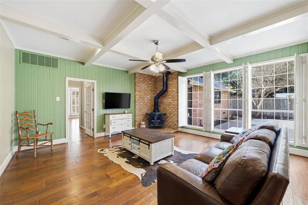 Living room with a wood stove, hardwood / wood-style flooring, coffered ceiling, a ceiling fan, and wooden walls