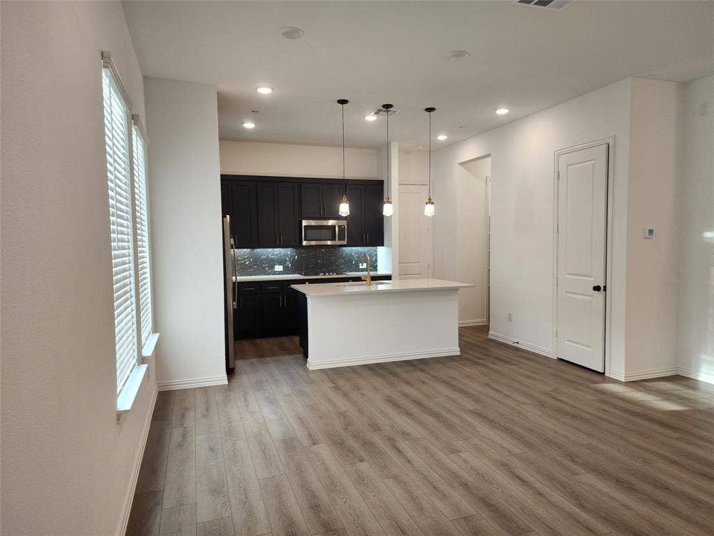 627 Redwood Way, Mansfield, TX 76063 Kitchen with dark cabinets, decorative light fixtures, tasteful backsplash, stainless steel microwave, and light wood-style floors