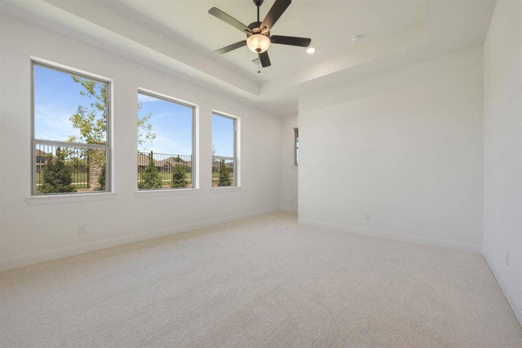 3283 Jersey Drive, Midlothian, TX 76065 Bright room featuring a tray ceiling with a built-in ceiling fan, three large windows, and neutral carpet flooring