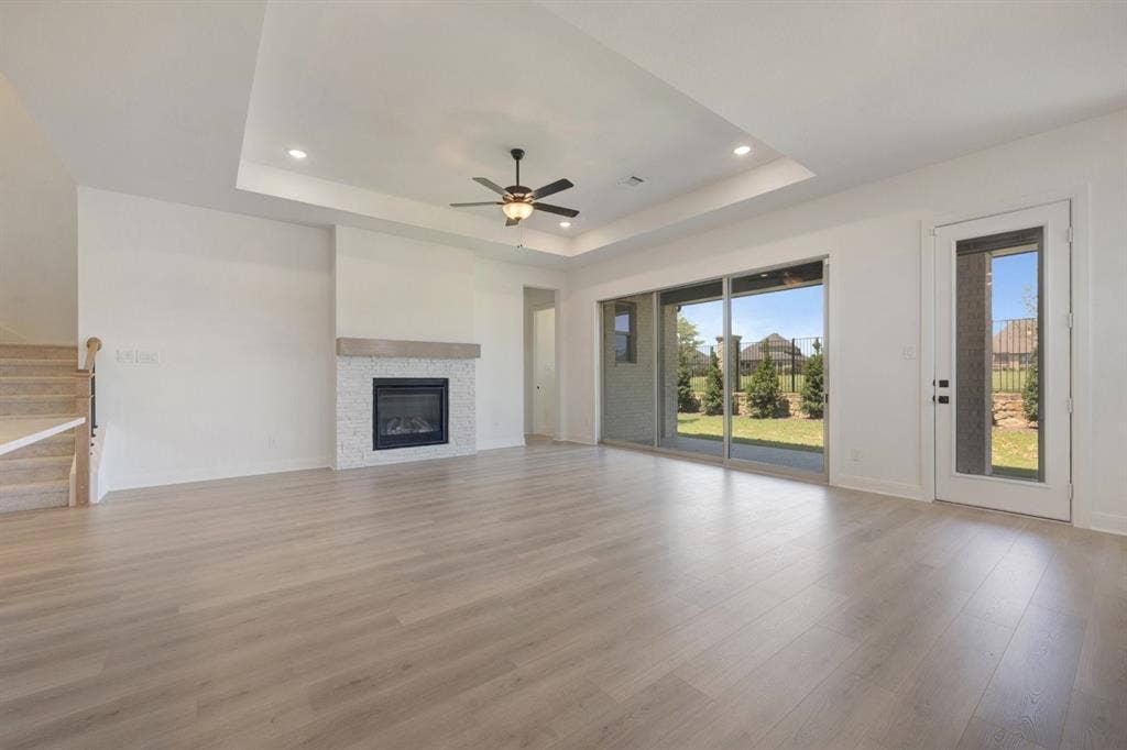 3283 Jersey Drive, Midlothian, TX 76065 Spacious living area featuring wood-finish flooring, a contemporary fireplace with white stacked stone and a wood mantel, a tray ceiling with recessed lighting, and a ceiling fan