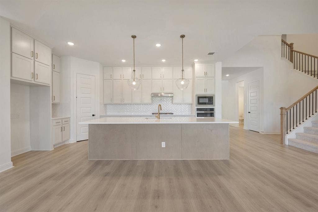 3283 Jersey Drive, Midlothian, TX 76065 Open-concept kitchen featuring an expansive island with a light-toned countertop, white cabinetry, a herringbone tile backsplash, and recessed lighting