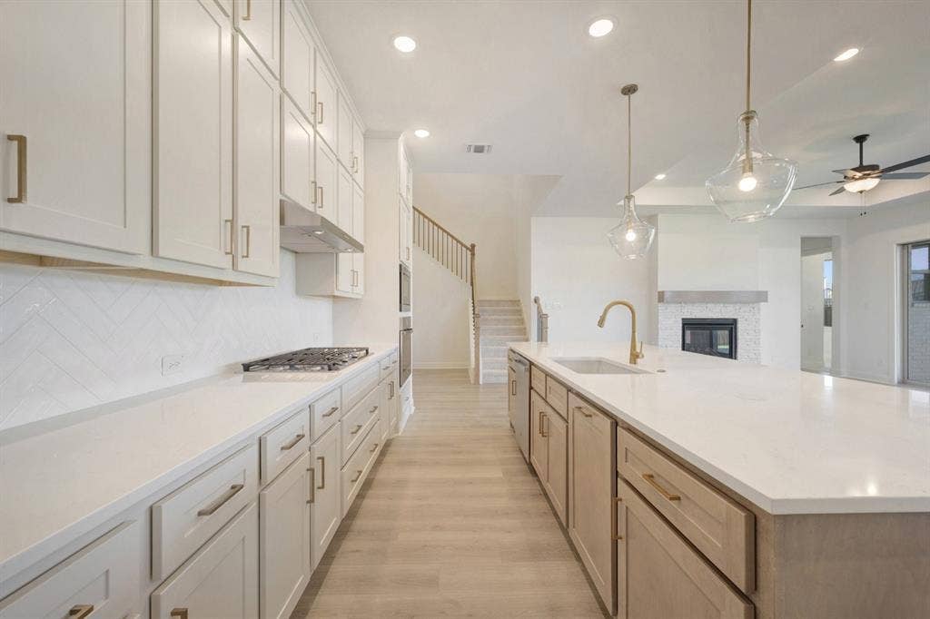 3283 Jersey Drive, Midlothian, TX 76065 Spacious kitchen featuring a large island with sink, white shaker cabinetry, stainless steel appliances, herringbone tile backsplash, and light wood-finish flooring