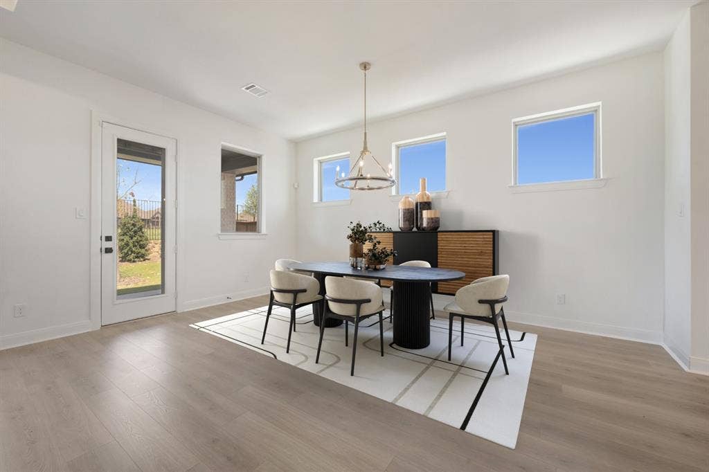 3283 Jersey Drive, Midlothian, TX 76065 Spacious room featuring light wood-finish flooring, multiple windows, a glass-paneled exterior door, and a suspended chandelier