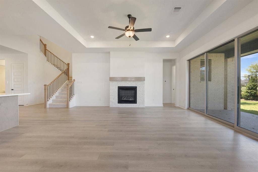 3283 Jersey Drive, Midlothian, TX 76065 Spacious living area featuring wood-finish flooring, a contemporary fireplace with stone tile surround and mantel, and a tray ceiling with recessed lighting and ceiling fan