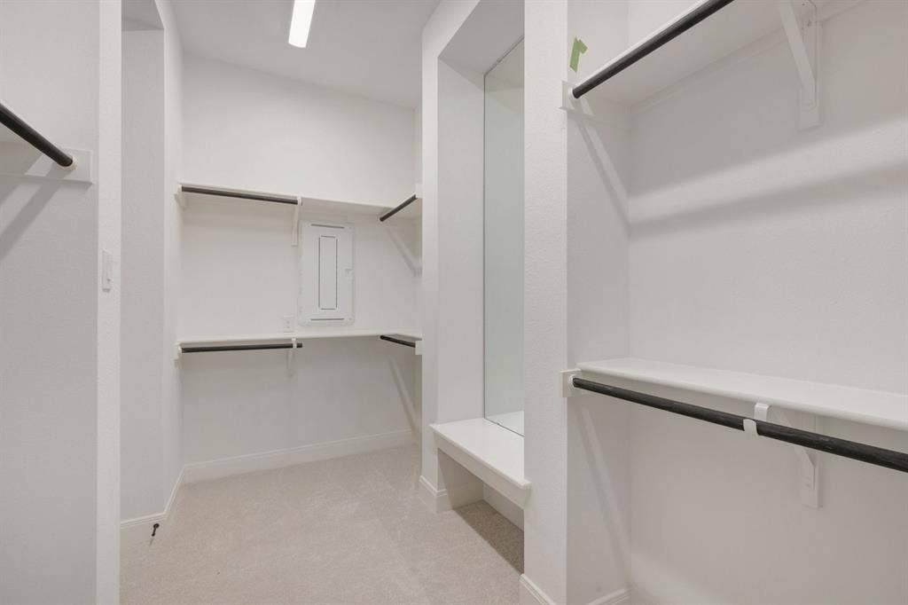 3283 Jersey Drive, Midlothian, TX 76065 Spacious walk-in closet featuring white shelving, matte black hanging rods, light-toned carpeting, and an integrated dressing bench with a full-length mirror