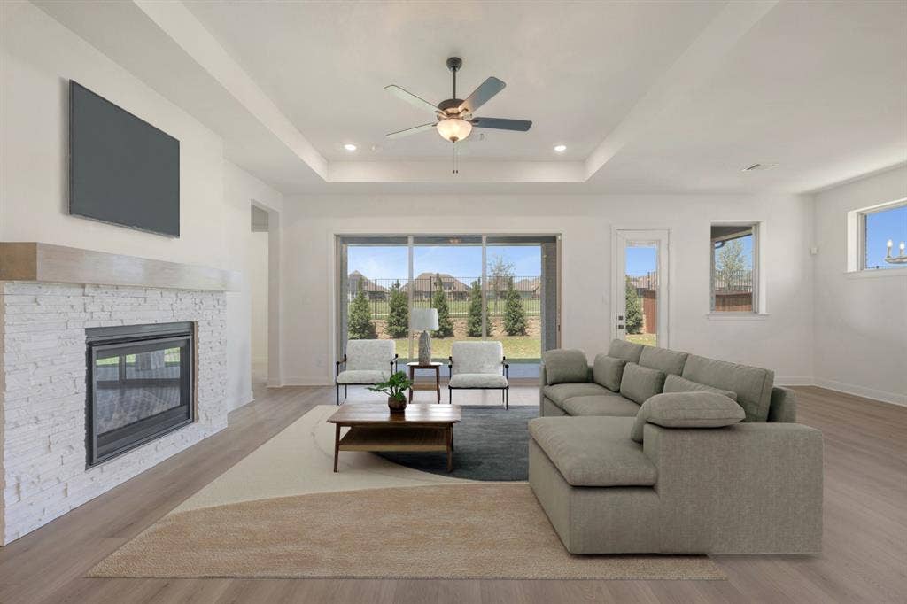 3283 Jersey Drive, Midlothian, TX 76065 Spacious living area featuring a stone-clad fireplace with a wood mantel, a ceiling fan with integrated lighting, and a tray ceiling