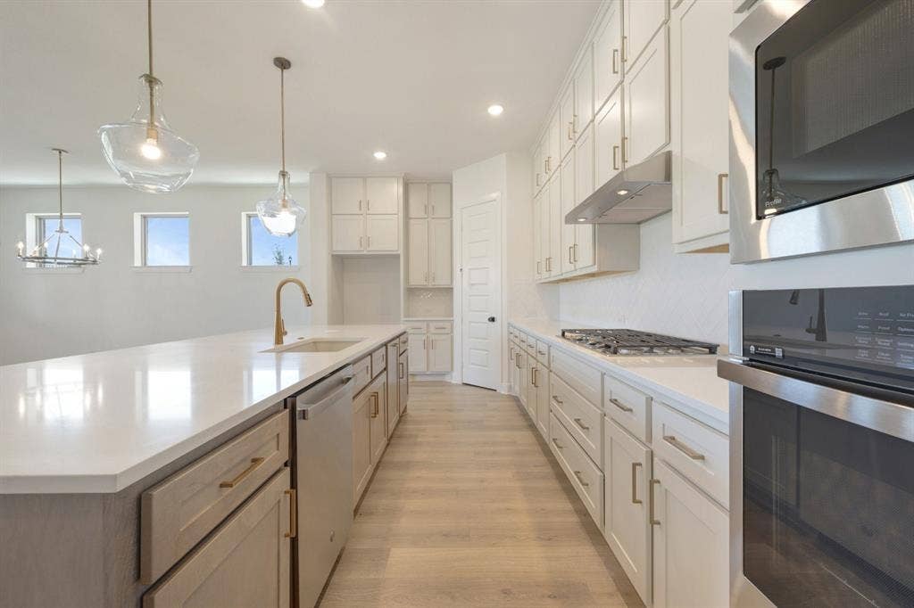 3283 Jersey Drive, Midlothian, TX 76065 Bright kitchen featuring a large island with sink, white shaker-style cabinetry, stainless steel appliances, light wood-finish flooring, and pendant lighting
