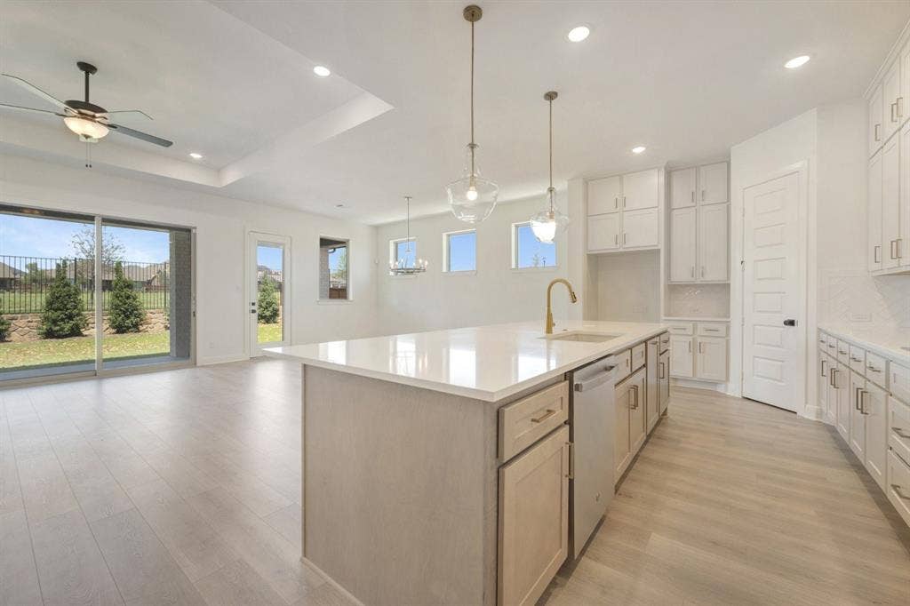 3283 Jersey Drive, Midlothian, TX 76065 Open-concept kitchen and living area featuring light wood-finish flooring, a kitchen island with a white countertop and integrated sink, pendant lighting, white cabinetry, and sliding glass doors to the exterior