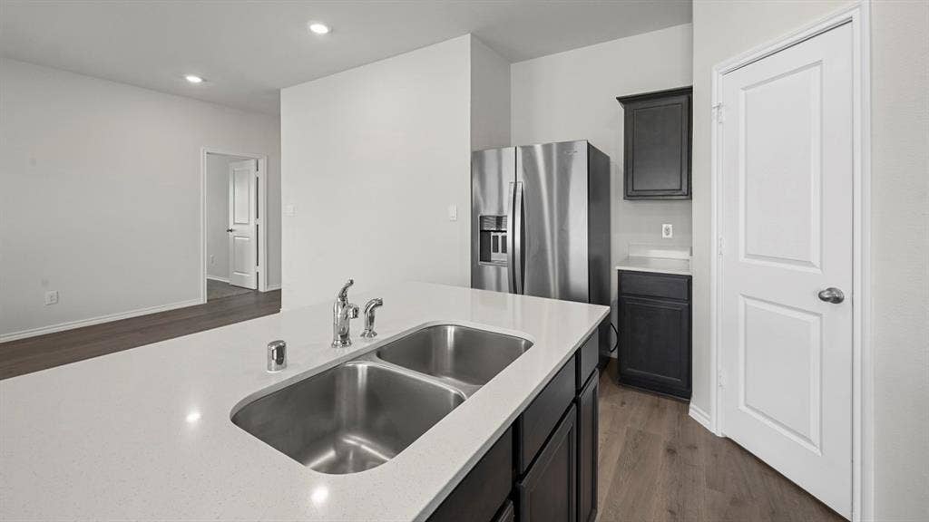 Kitchen featuring dark cabinetry, dark wood-style flooring, stainless steel fridge with ice dispenser, recessed lighting, and light stone countertops