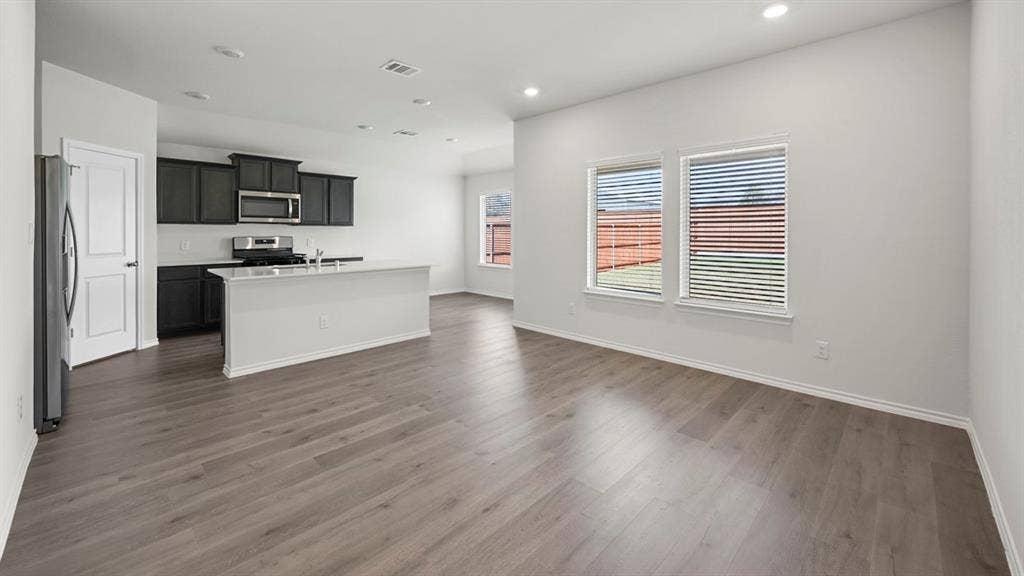 Kitchen featuring a kitchen island with sink, open floor plan, stainless steel appliances, recessed lighting, and dark wood-type flooring